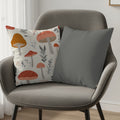 Two decorative throw pillows on a grey armchair, one with a mushroom pattern, the other solid grey.
