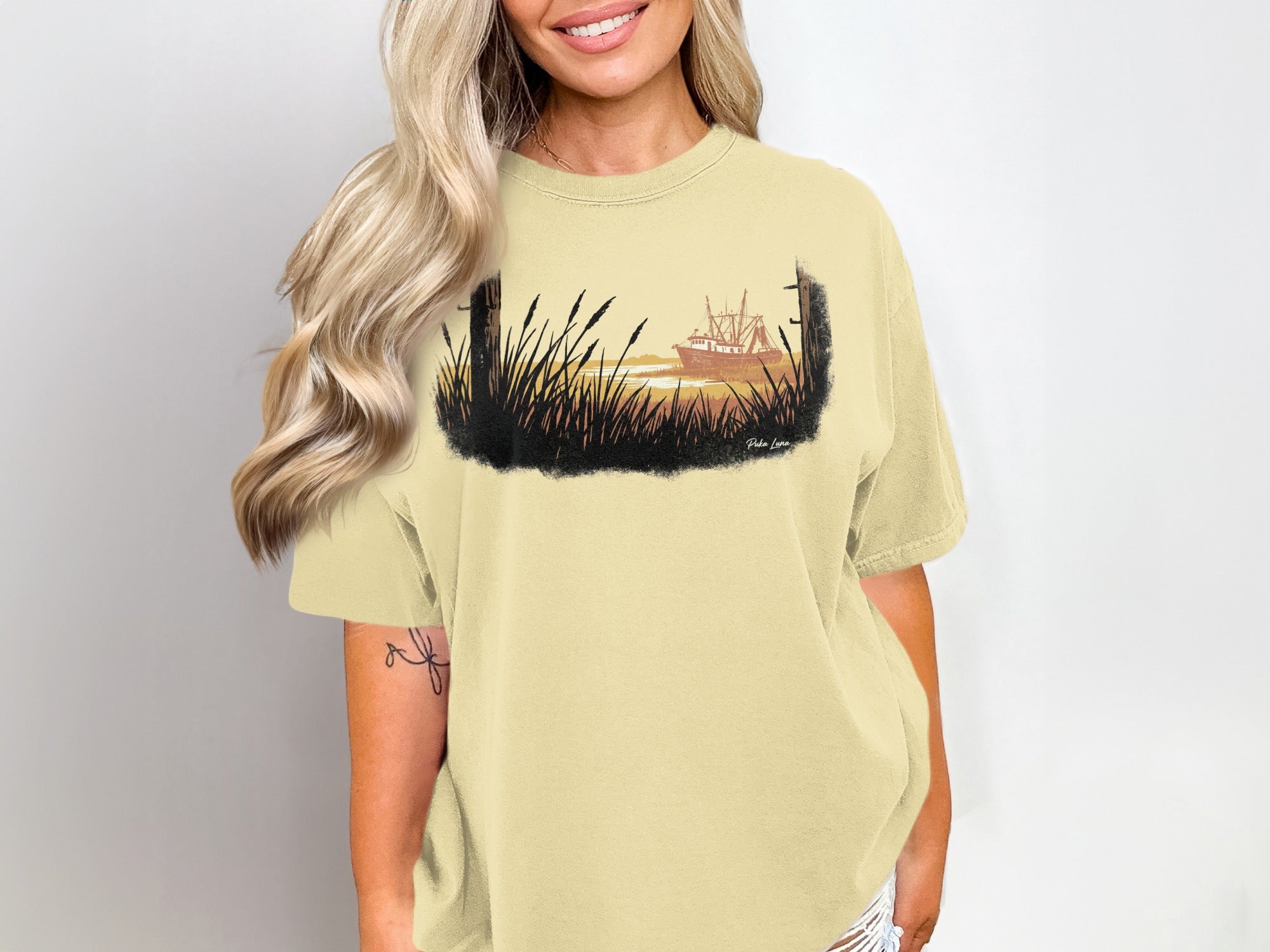 T-shirt with watercolor graphic of a shrimp boat at sunset among tall grass.