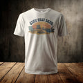 White t-shirt with graphic of campfire scene at sunset with text "STAY PAST DARK".