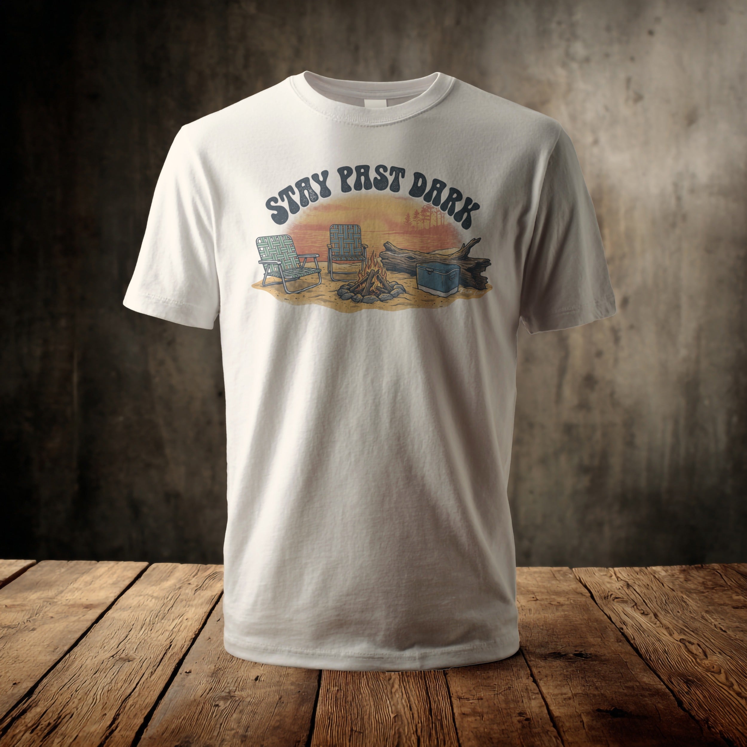 White t-shirt with graphic of campfire scene at sunset with text "STAY PAST DARK".