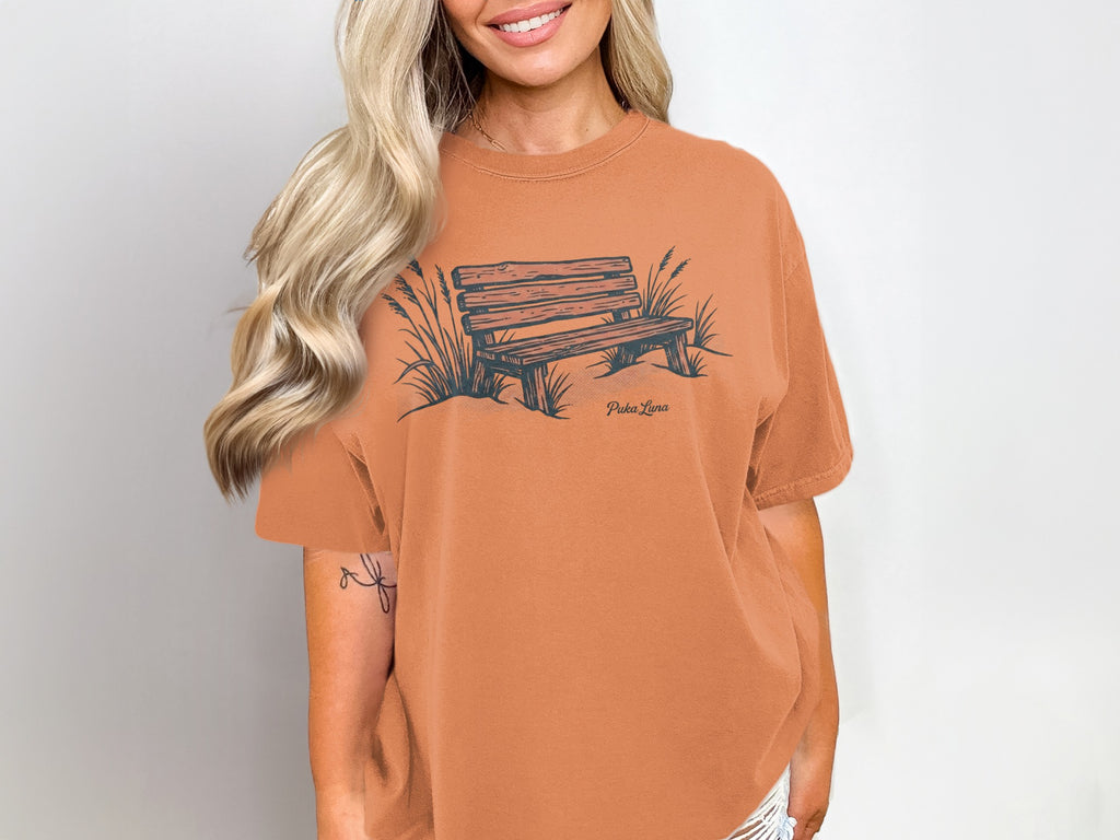 Orange t-shirt with a graphic of a wooden park bench and grass.