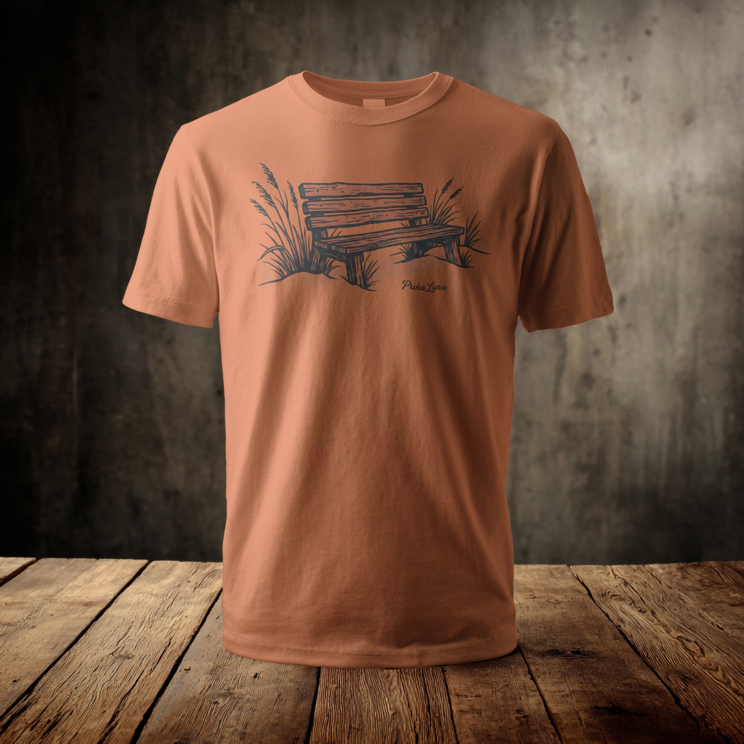 Orange t-shirt with a sketch of a wooden park bench and grass.