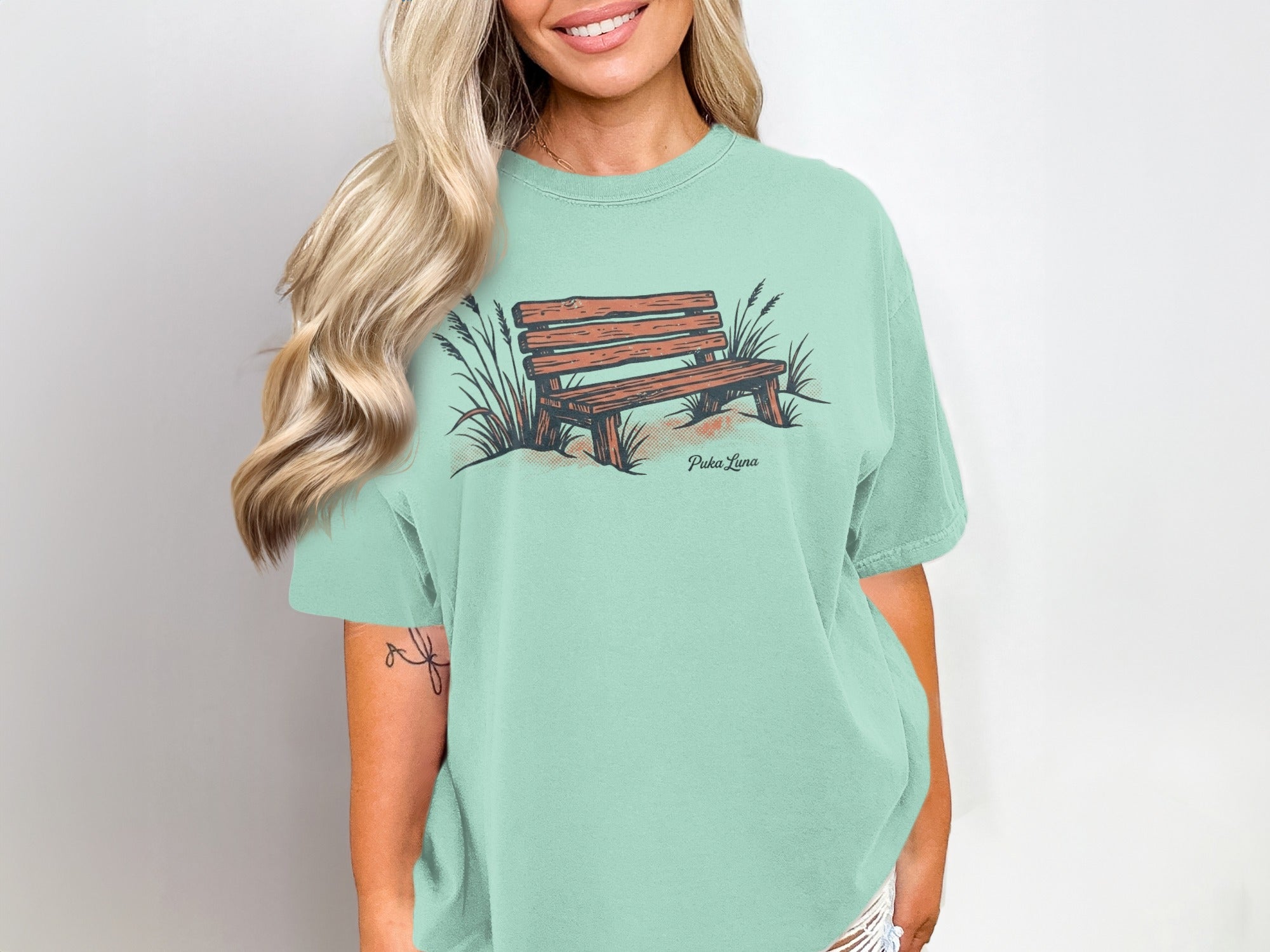 Light teal t-shirt with a graphic of a wooden bench and grass.