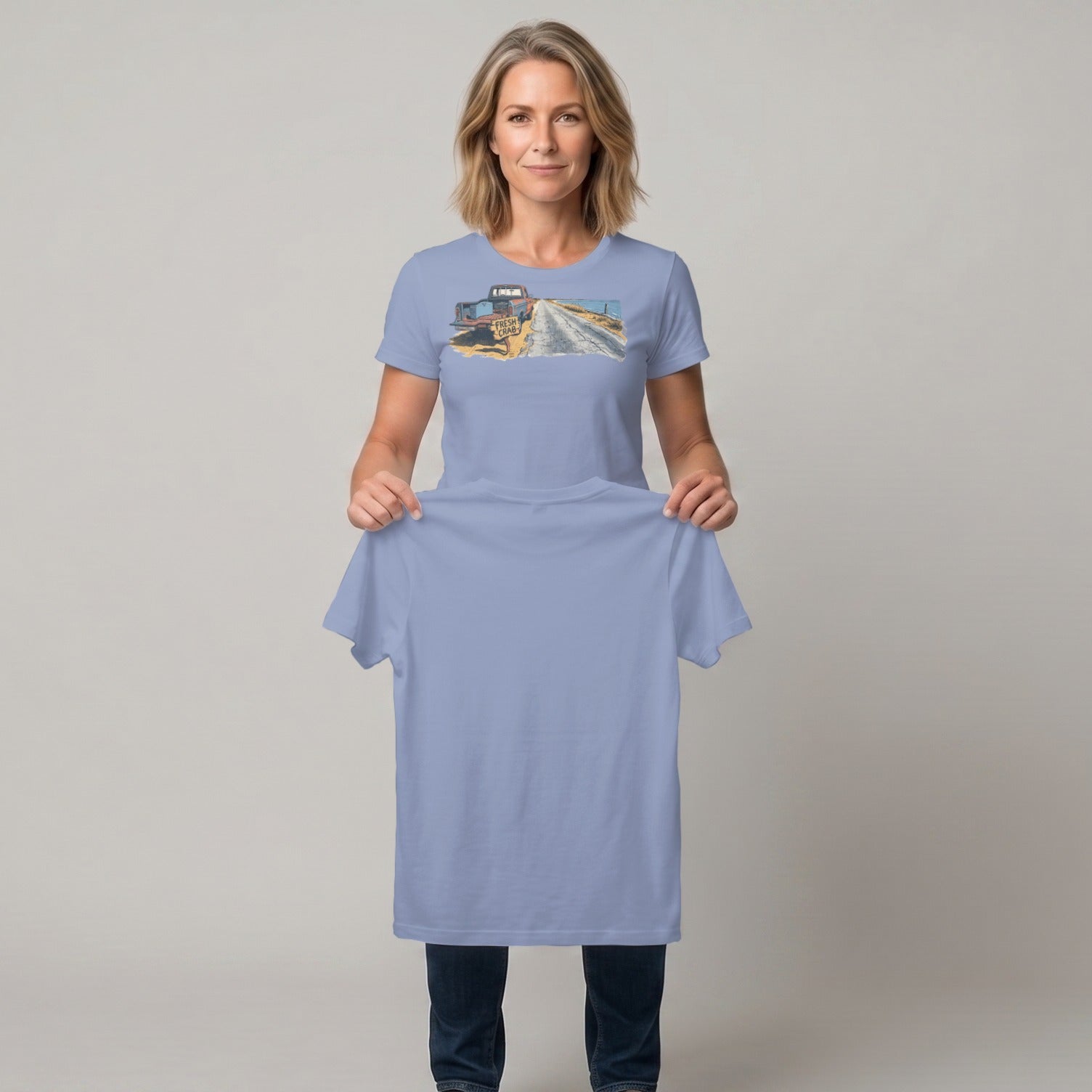 Woman holding light blue t-shirt with printed graphic of a vintage truck on a dirt road.