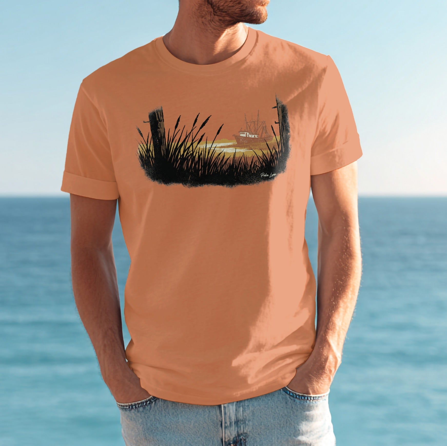 Orange t-shirt featuring a printed silhouette of a ship sailing at sea behind tall grass.