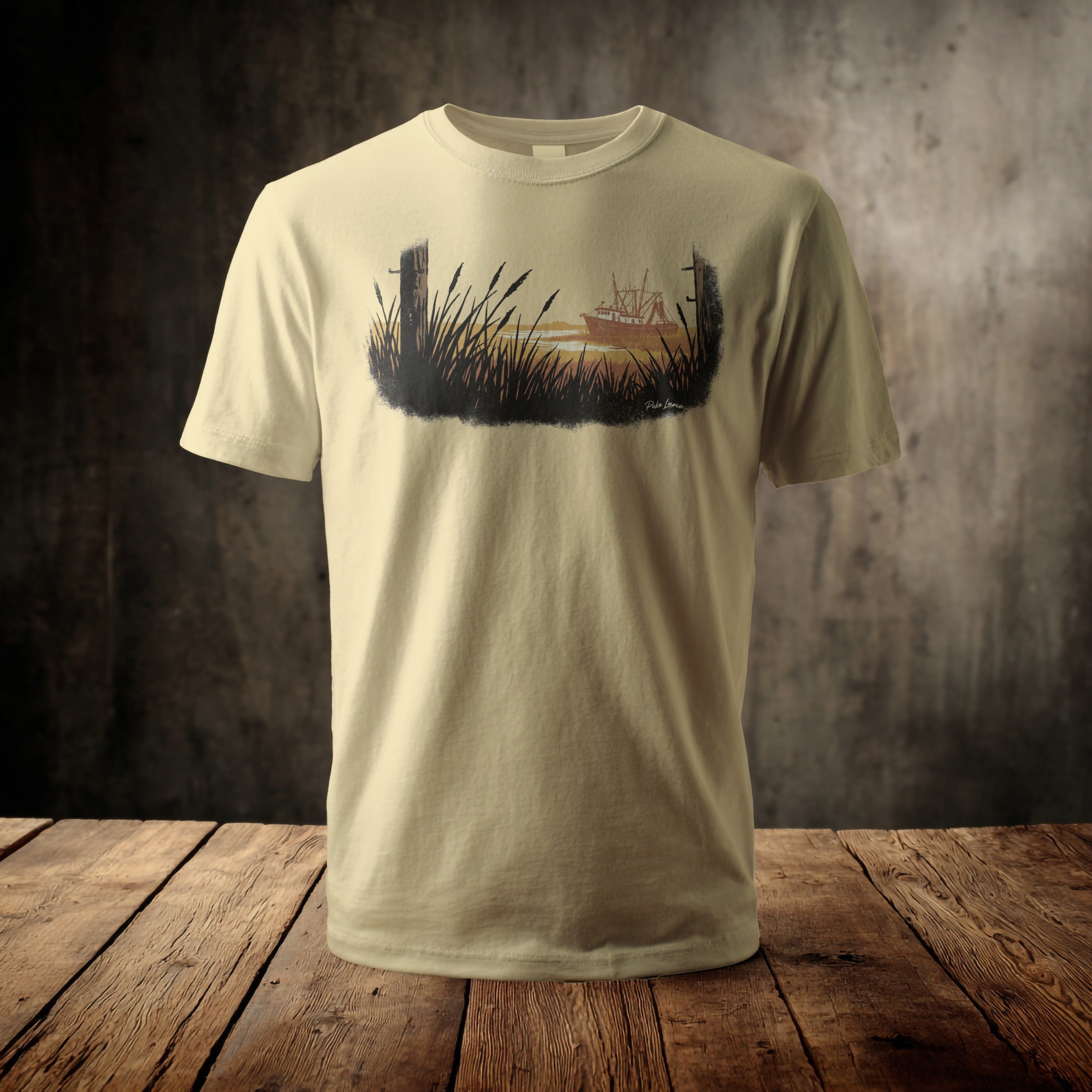 Light tan t-shirt with a dark silhouette design of a boat in tall grass.