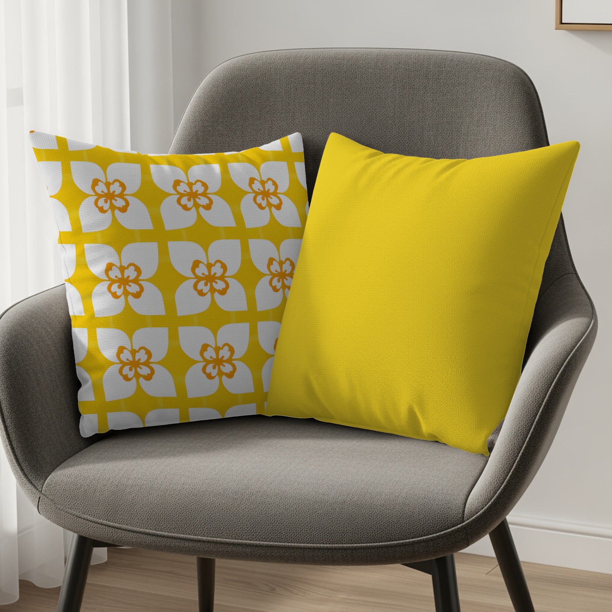 Two decorative throw pillows on a gray chair, one with a white floral pattern, one solid yellow.
