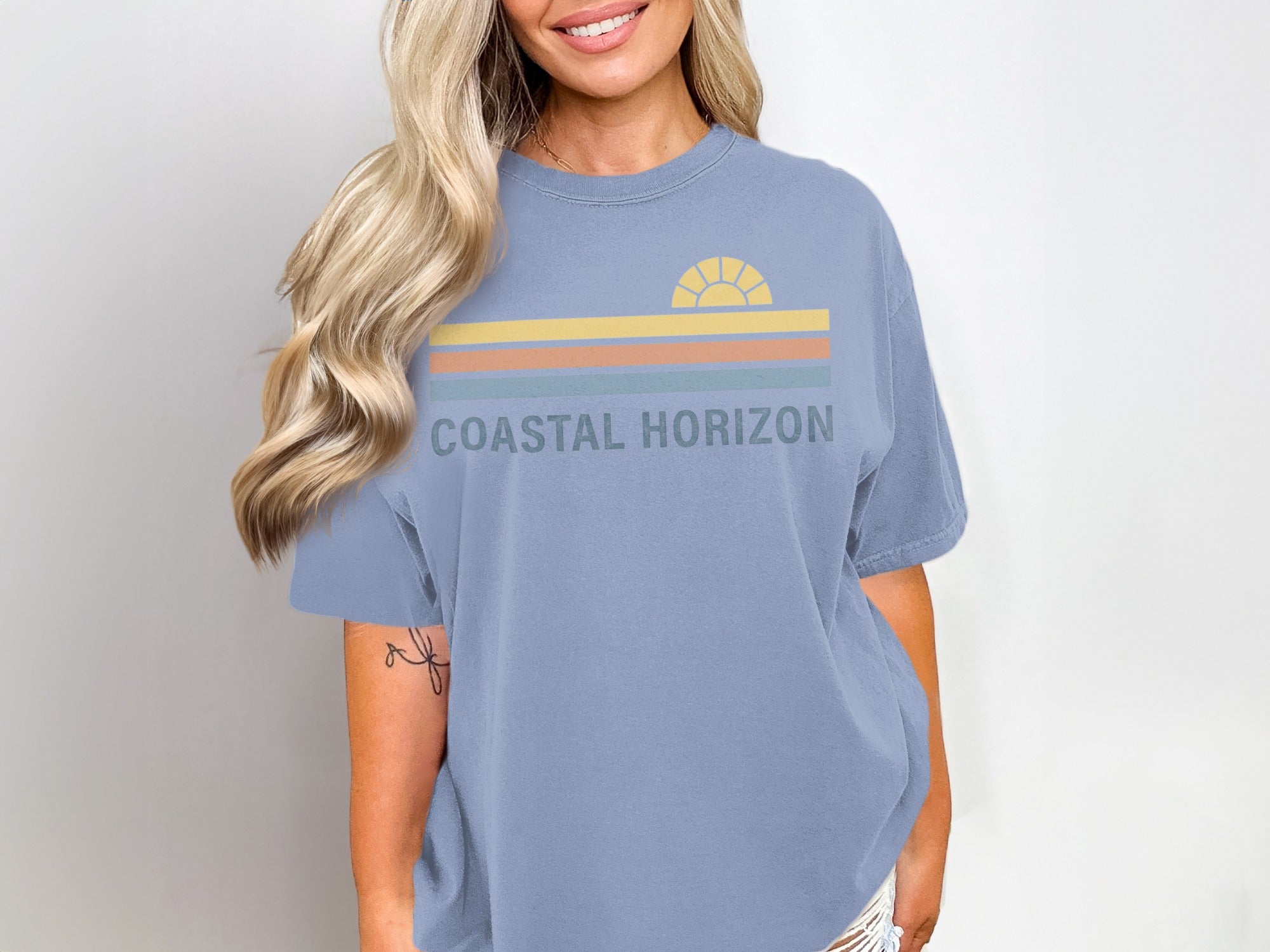 Blue t-shirt with "COASTAL HORIZON" text and a striped sunset graphic.