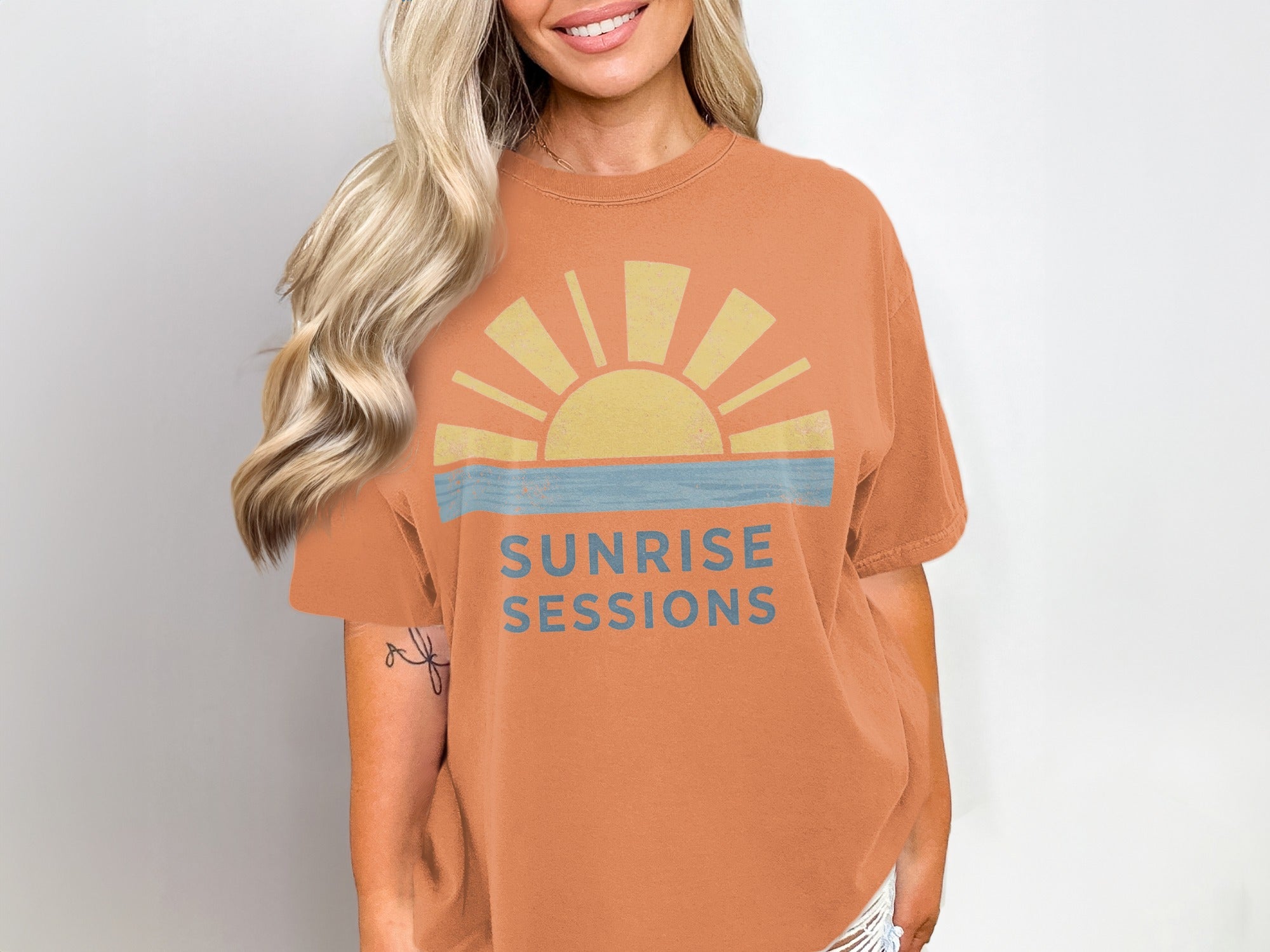 Orange t-shirt with a yellow sun and blue stripes saying "Sunrise Sessions".
