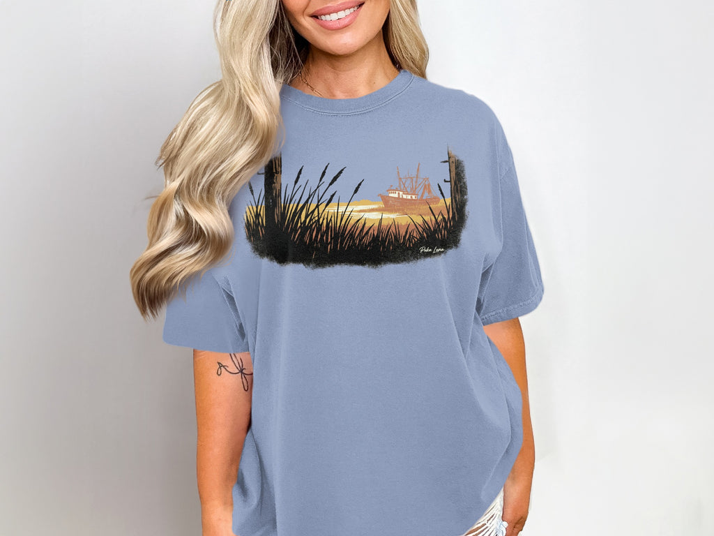 Woman wearing a faded blue t-shirt with a coastal fishing boat illustration.