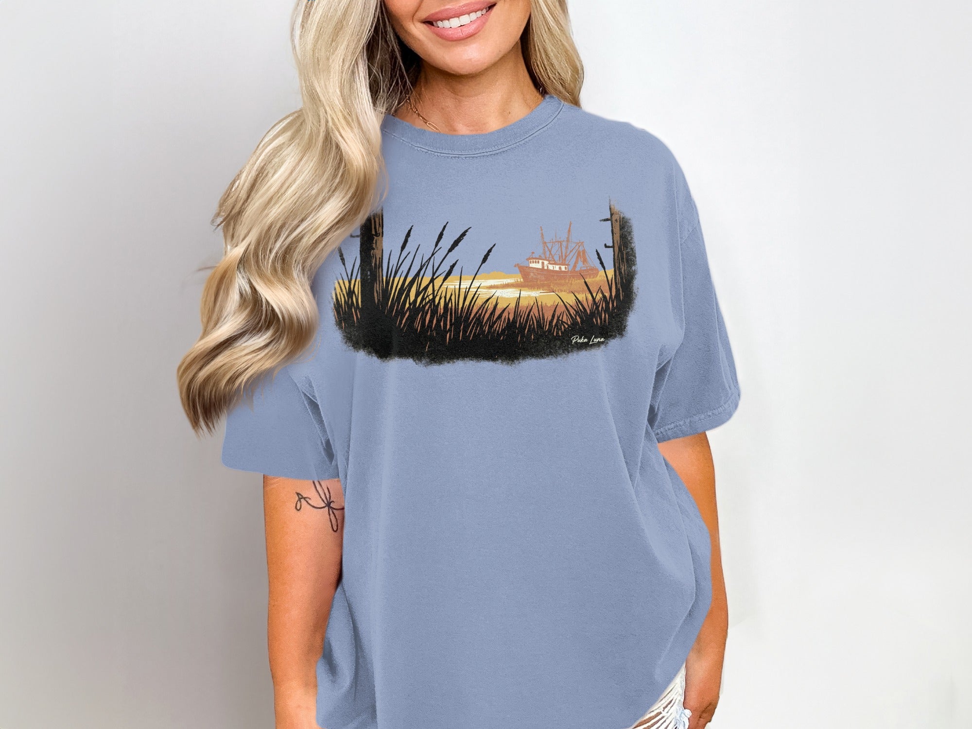 Woman wearing a faded blue t-shirt with a coastal fishing boat illustration.
