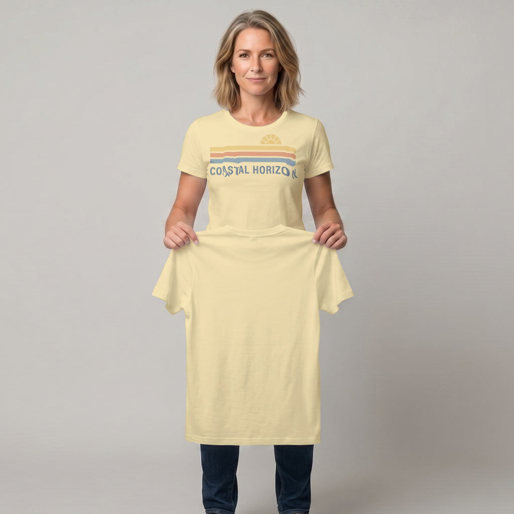Woman holding a light yellow t-shirt with a retro sunset design and "COASTAL HORIZON" text.