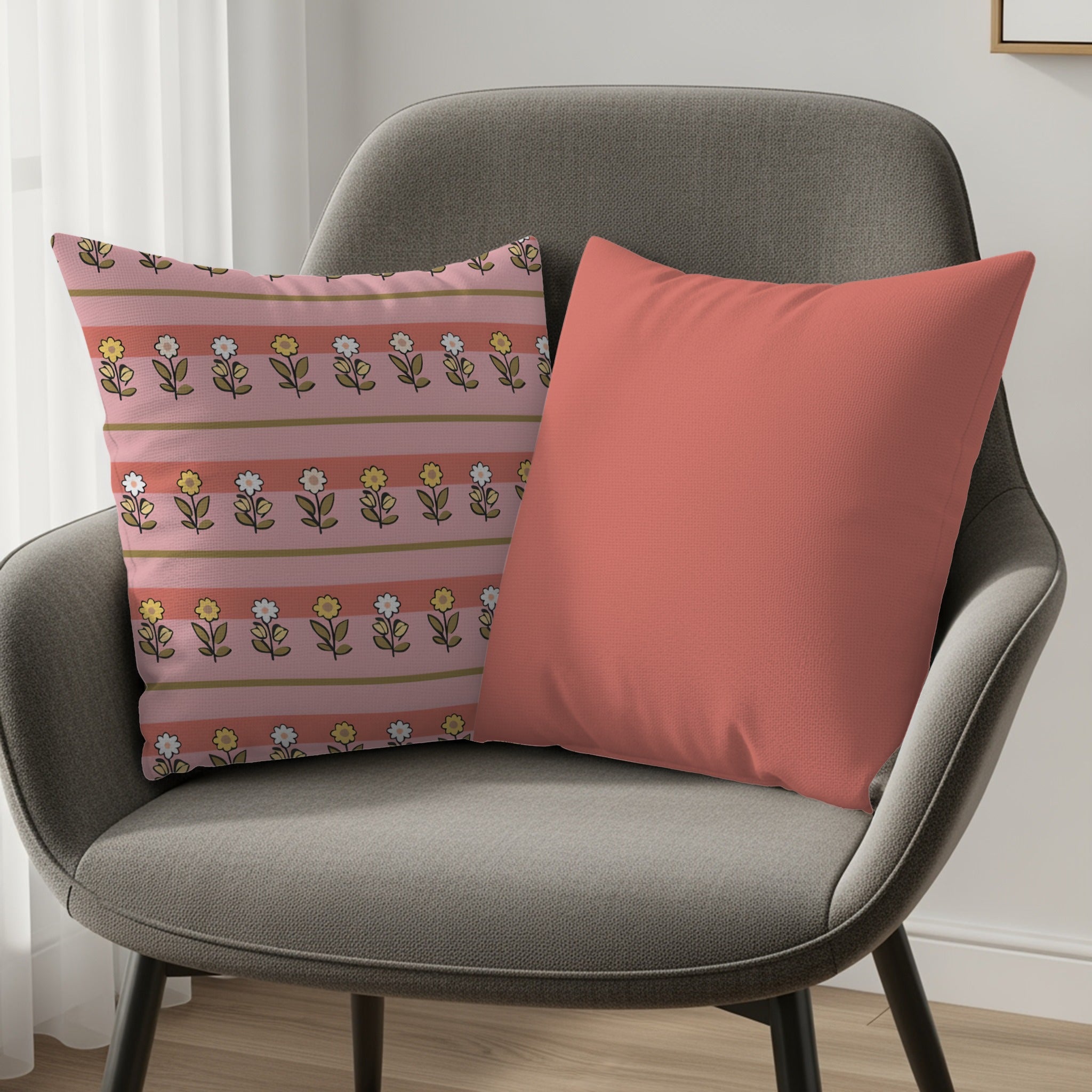 Two decorative throw pillows on a gray armchair, one with a floral stripe pattern.