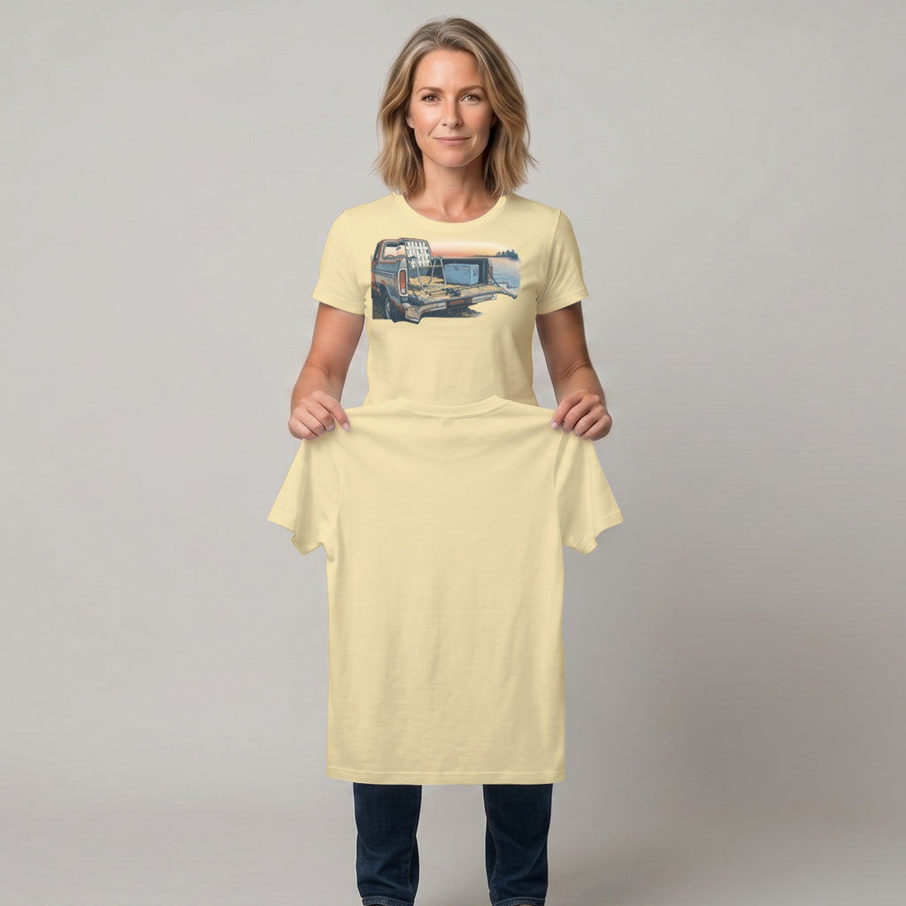 Woman holding a pale yellow t-shirt with a truck at sunset graphic.