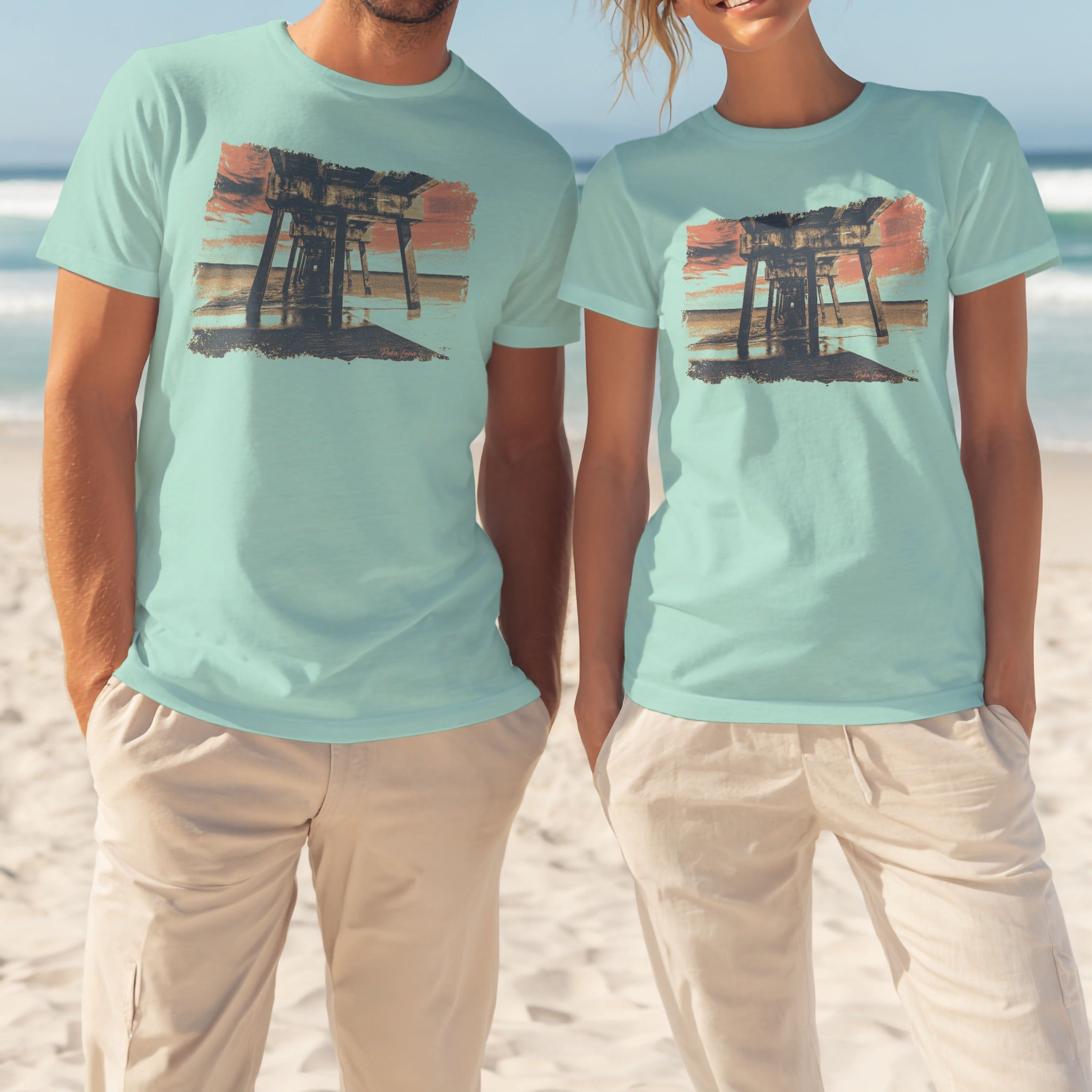 Two models wear light blue t-shirts featuring a wooden pier at sunset.